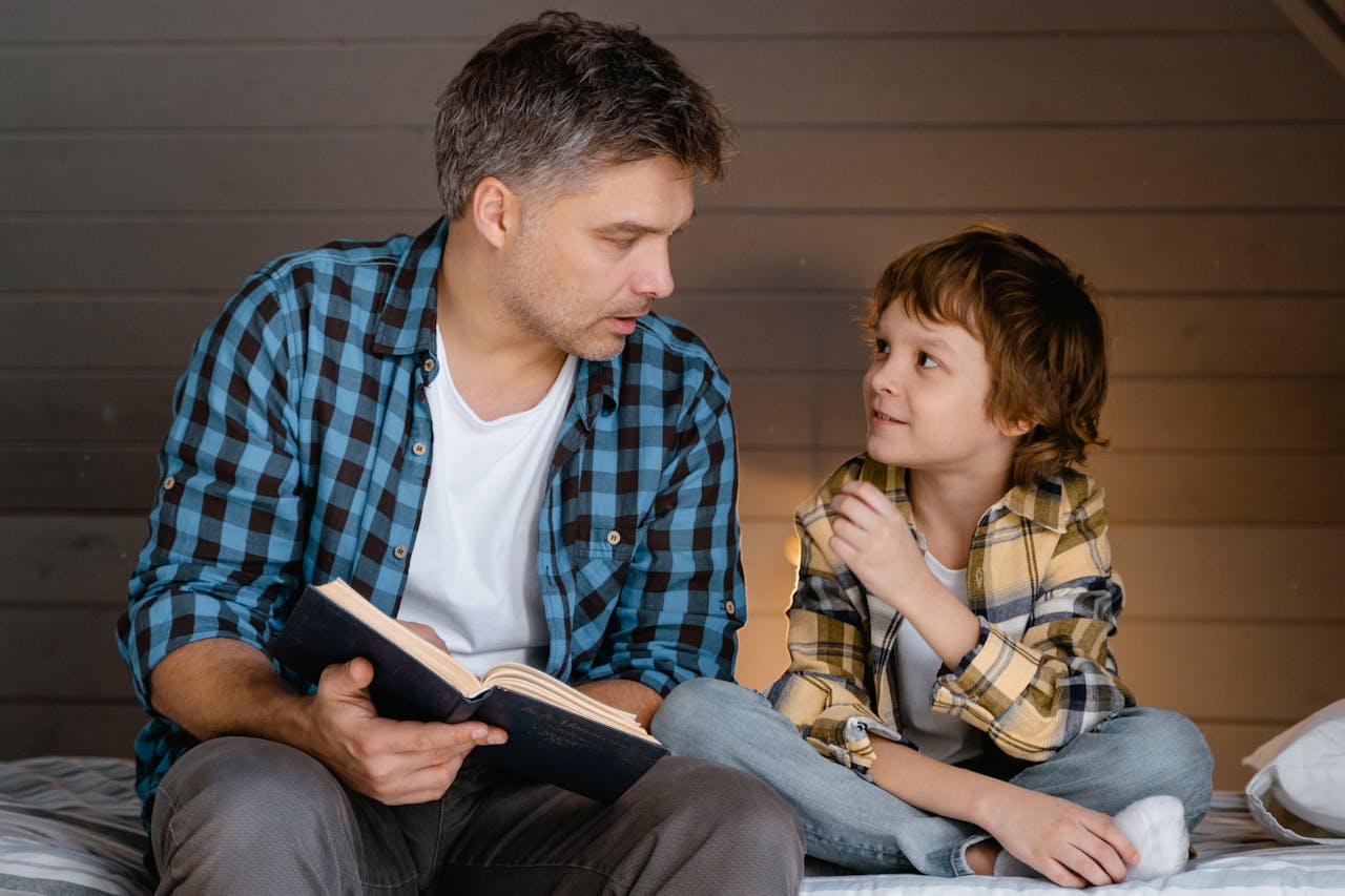 A father and son share a bonding moment reading together indoors, fostering family connection.